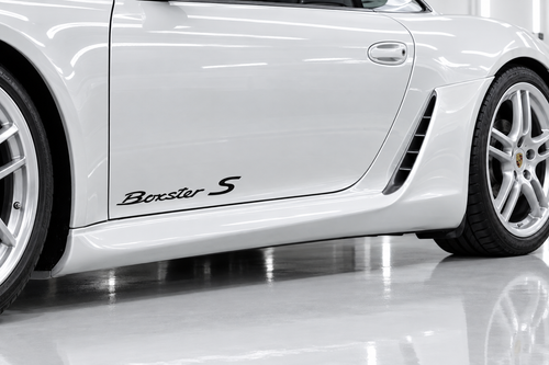 Illustrative mockup of black Boxster S door decals on a white Porsche Boxster 987 in a bright detailing garage.