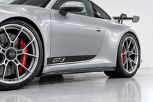 Illustrative mockup of a black GT3 lower door stripe on a silver Porsche 992 GT3, viewed from a close front oblique angle.